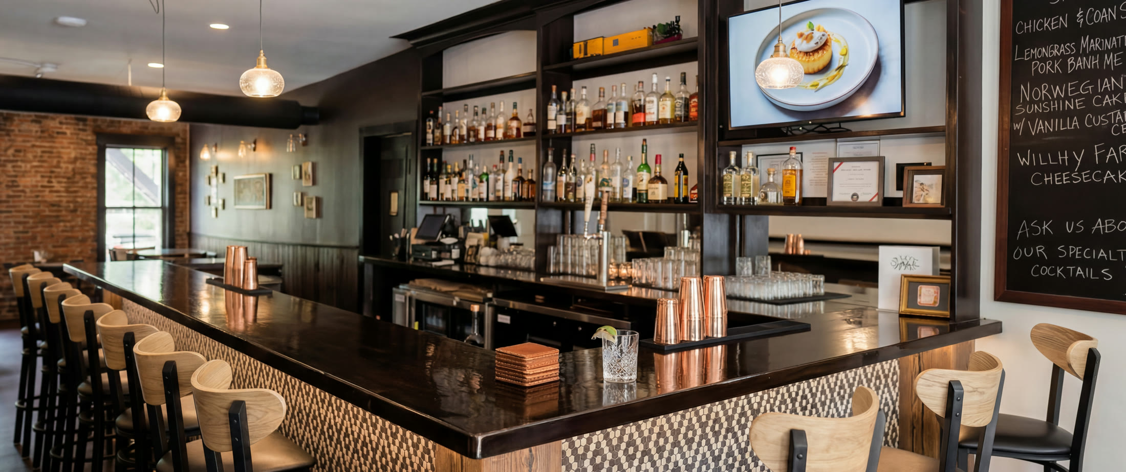 Warm interior bar at Sal's Tavern with stools, bottles, chalkboard specials, and pendant lights